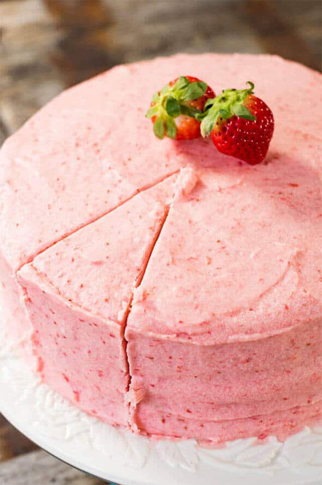 A close up of a strawberry cake with one slice cut