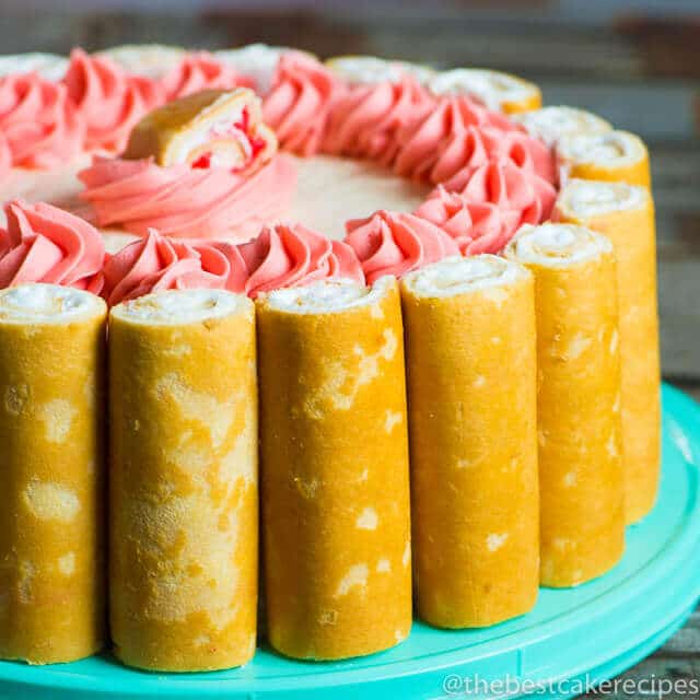 Easy, semi-homemade strawberry shortcake cake with white cake, white buttercream and strawberry buttercream accents. This simply flavored cake is beautifully decorated with strawberry shortcake roll snacks.