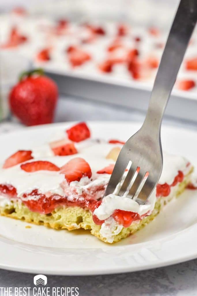 piece of sheet cake with strawberries on a plate with a fork
