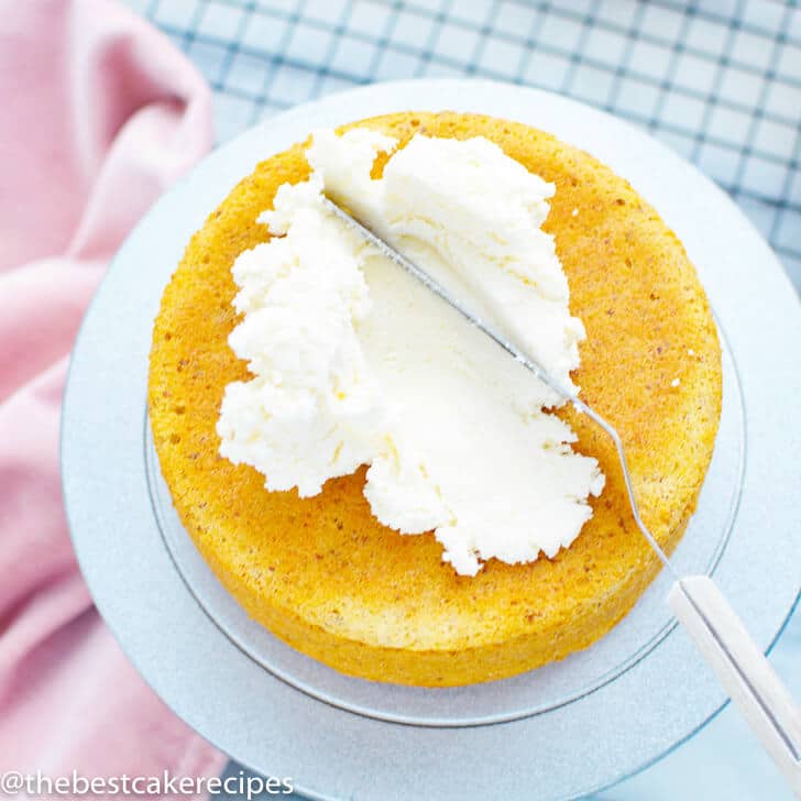 spreading white frosting on a yellow cake