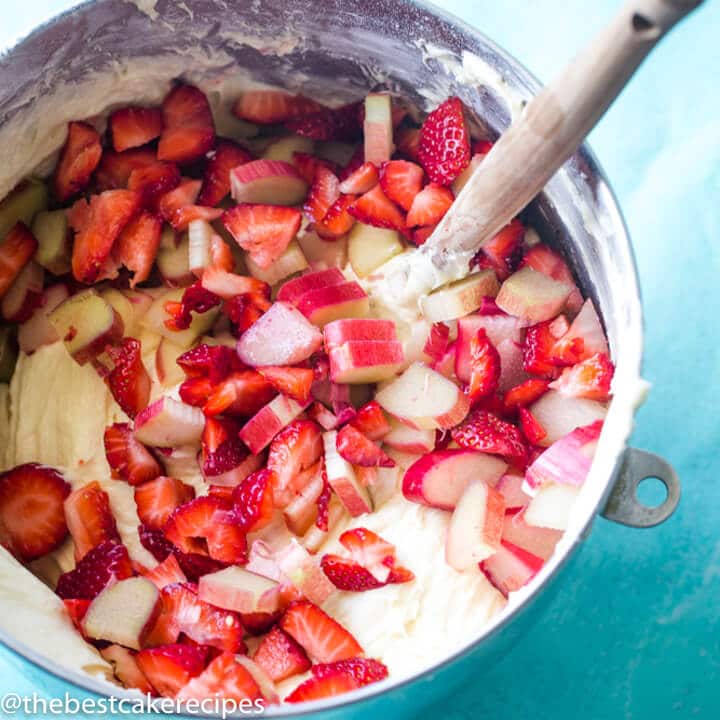 bundt cake batter with strawberries and rhubarb in a mixing bowl