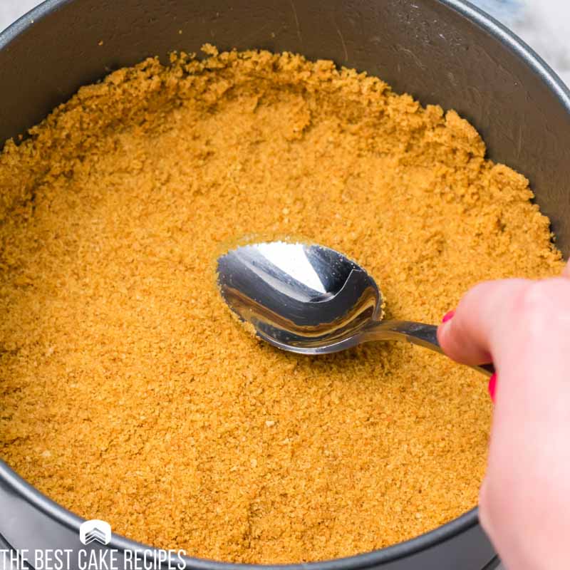 spoon pressing graham cracker crust in a springform pan