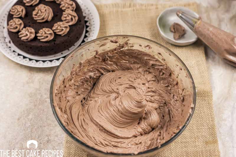 bowl of chocolate frosting with a chocolate cake in the background