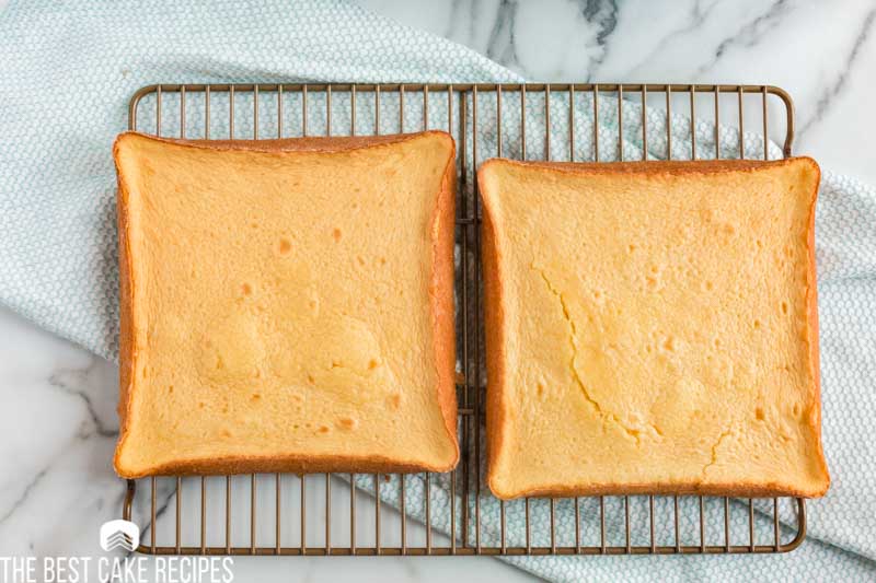 two square yellow cakes cooling on a wire rack