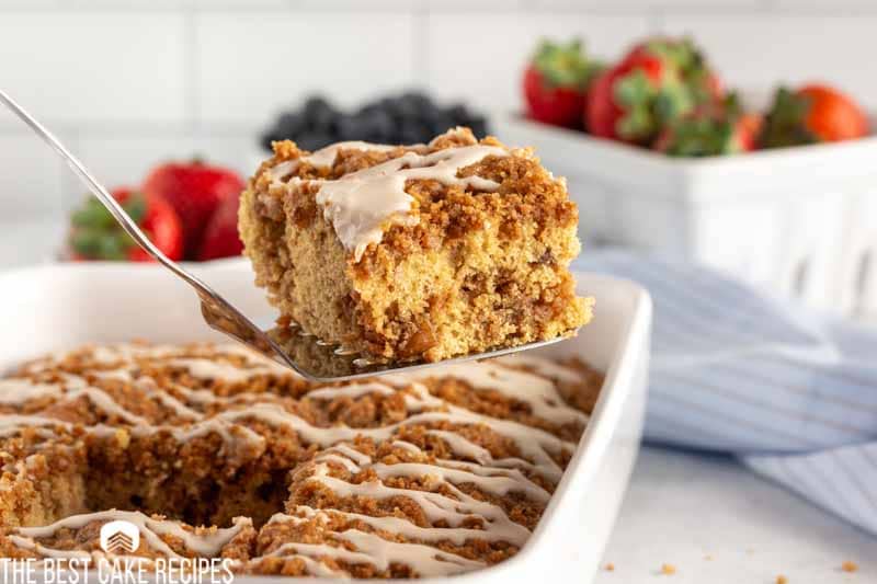 piece of coffee cake on a spatula with fruit in the background