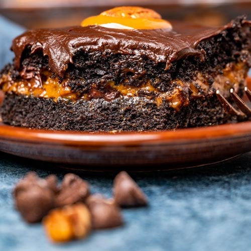 slice of caramel chocolate turtle cake on a plate with a bite out