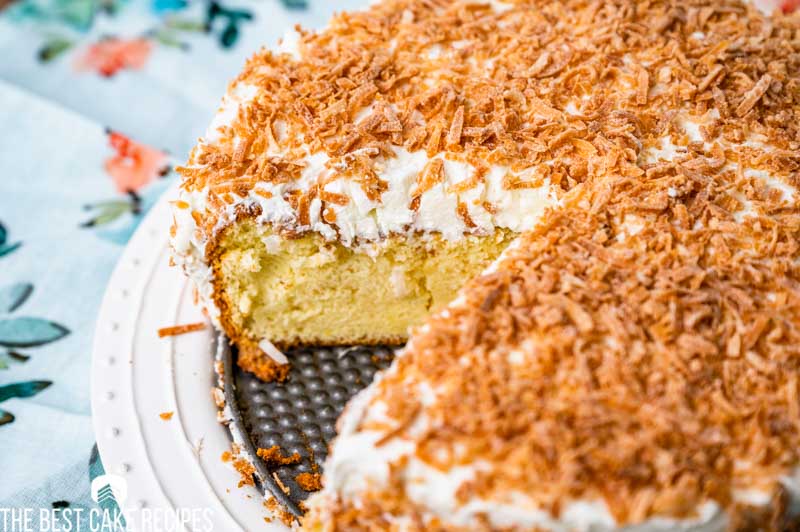 a coconut tres leches cake on a plate with one slice missing