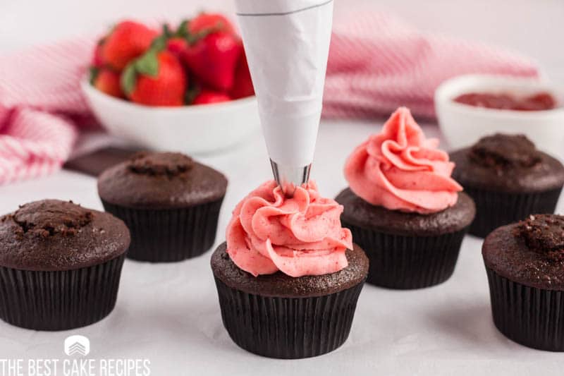 piping strawberry frosting on a chocolate cupcake