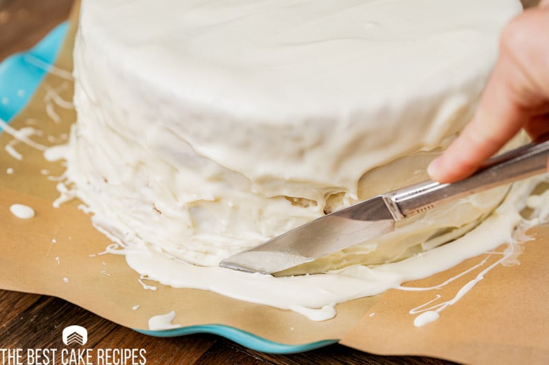knife cutting white chocolate around bottom of cake