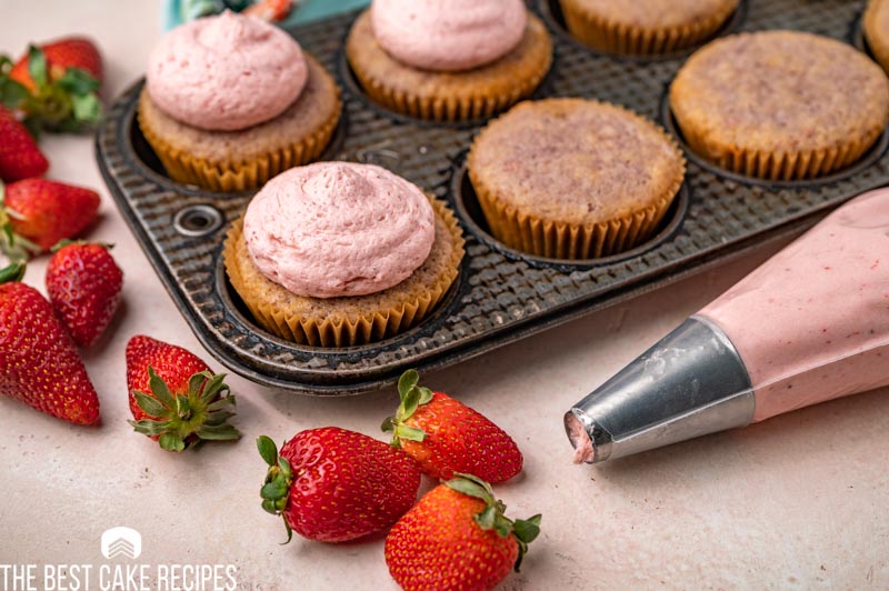 strawberry cupcakes in a muffin pan, half with frosting