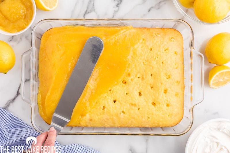 spreading lemon curd on a poke cake