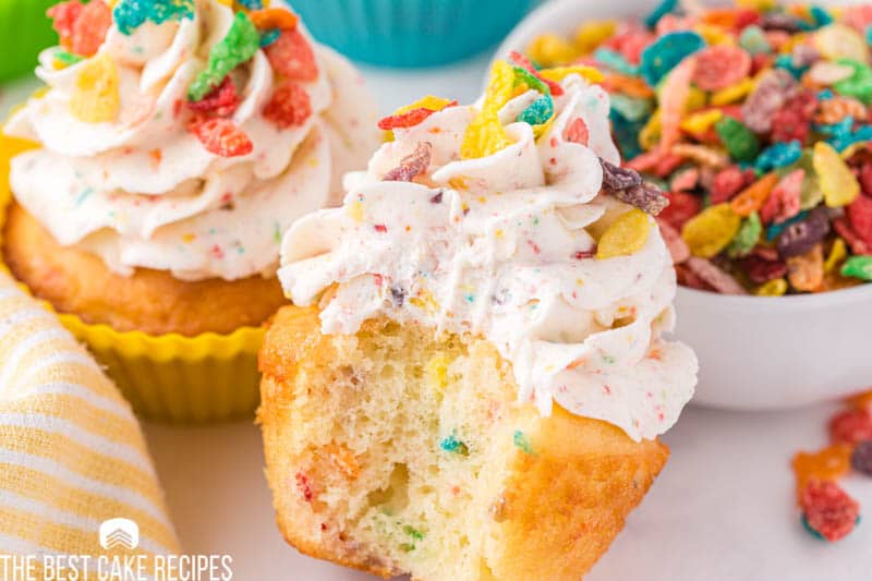 a closeup of a fruity pebble cupcake with one bite missing