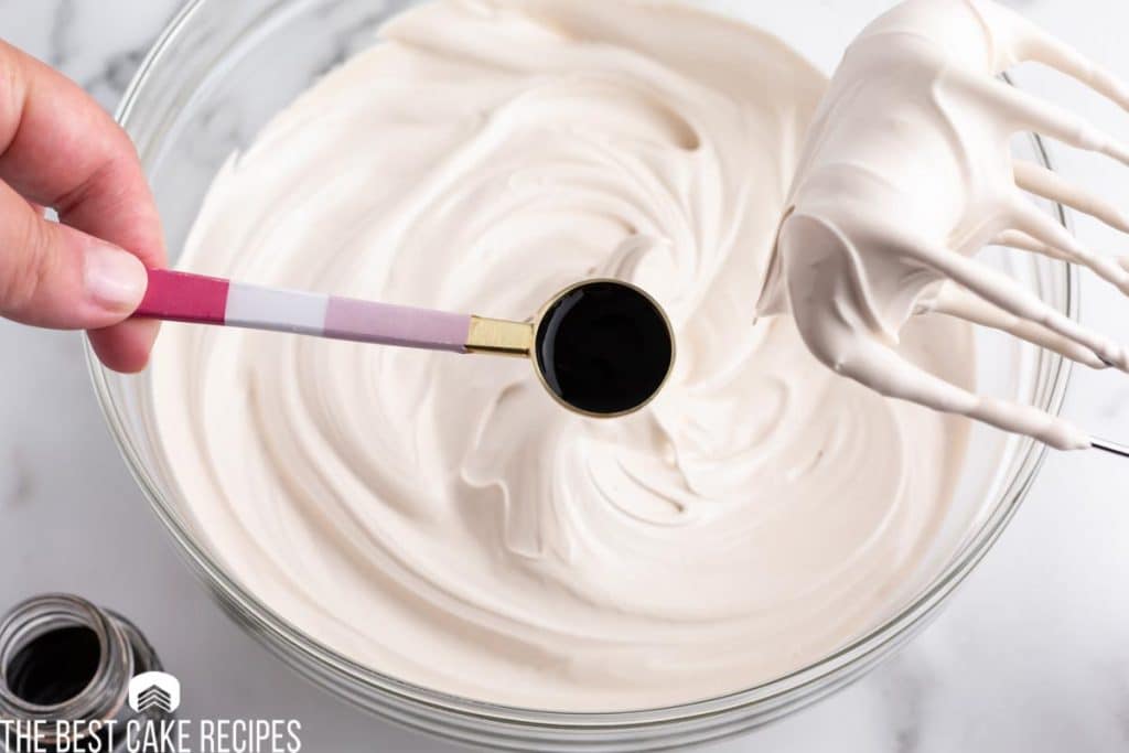 vanilla extract in a teaspoon over a bowl of frosting