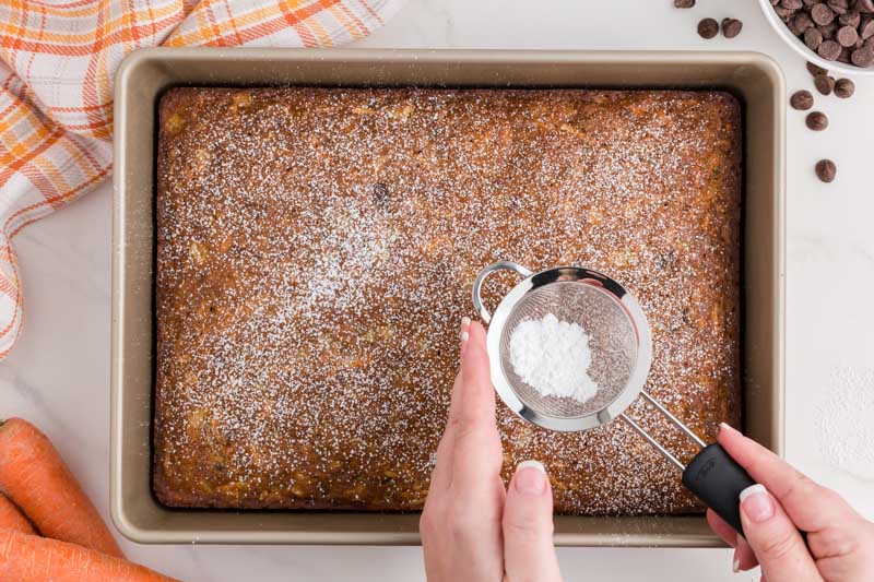 shaking powdered sugar over a carrot cake