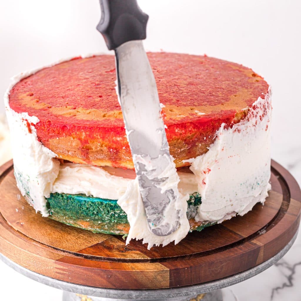 a cake spatula spreading white frosting on a cake