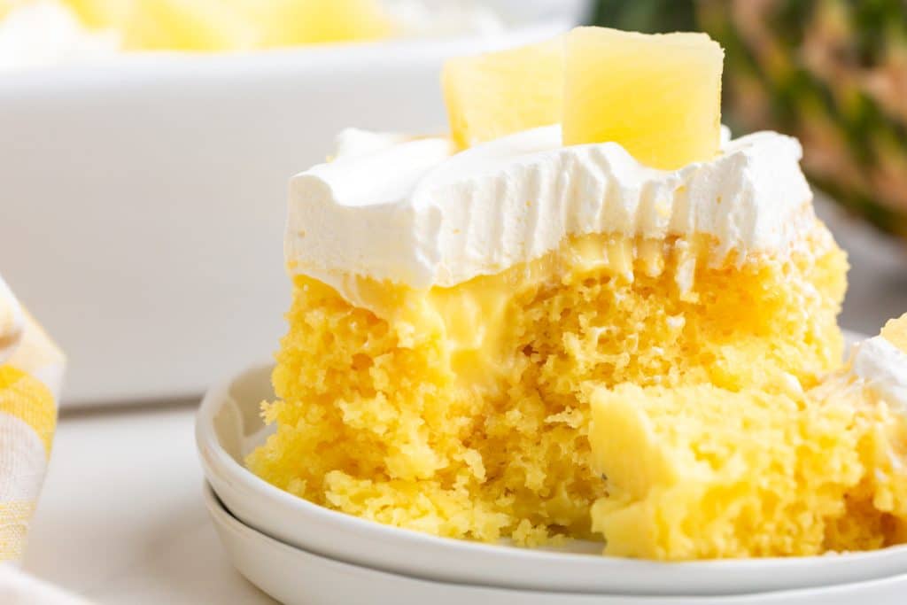 closeup of a piece of pineapple poke cake with a bite out on a plate