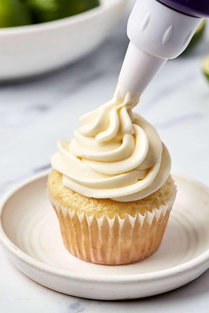 piping a swirl of frosting on a cupcake