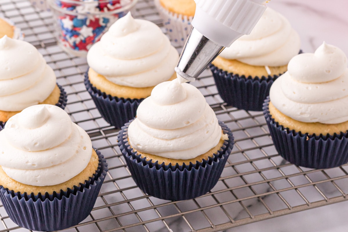 piping white frosting on a cupcake
