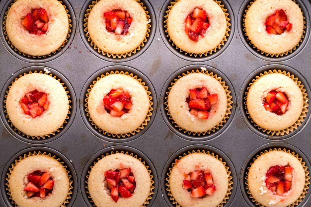 white cupcakes with strawberry filling in a cupcake pan