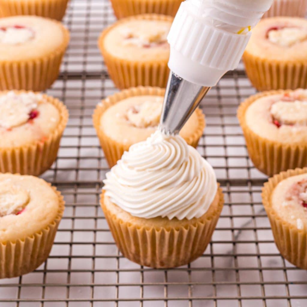 piping a swirl of vanilla frosting on a cupcake
