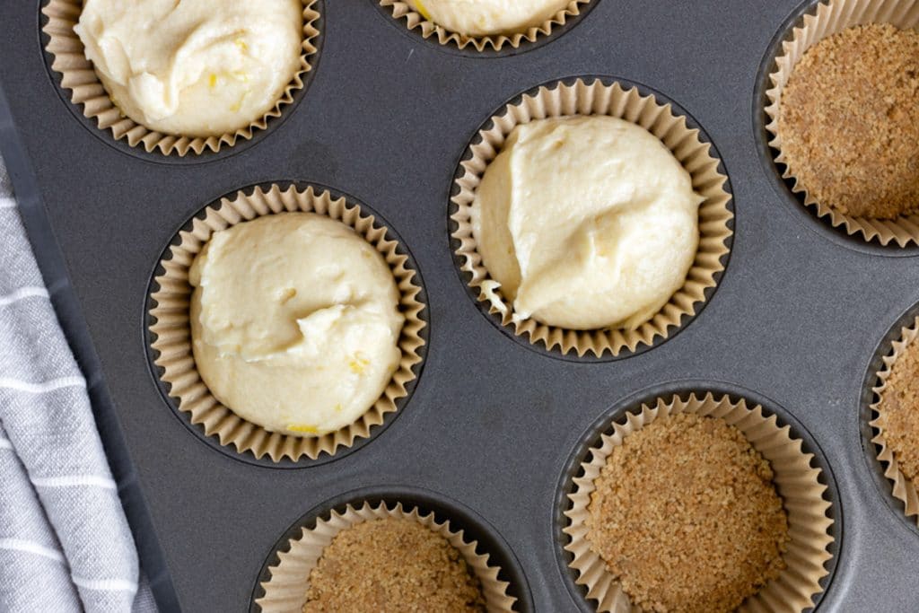 cupcake batter on graham cracker crusts in a muffin pan