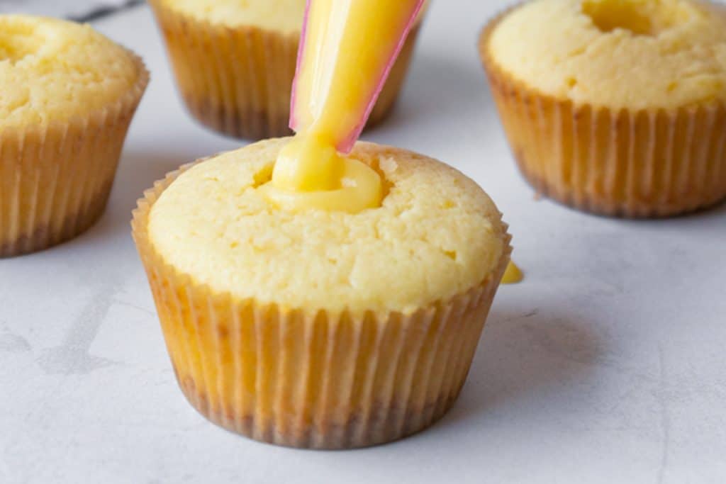 piping lemon curd into the center of a cupcake