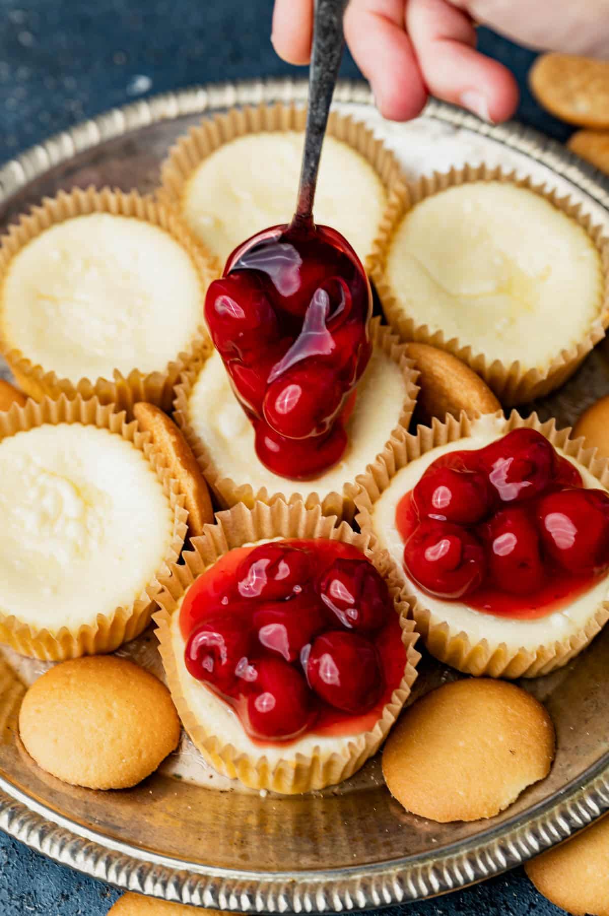 spooning cherry pie filling on mini cheesecake cups