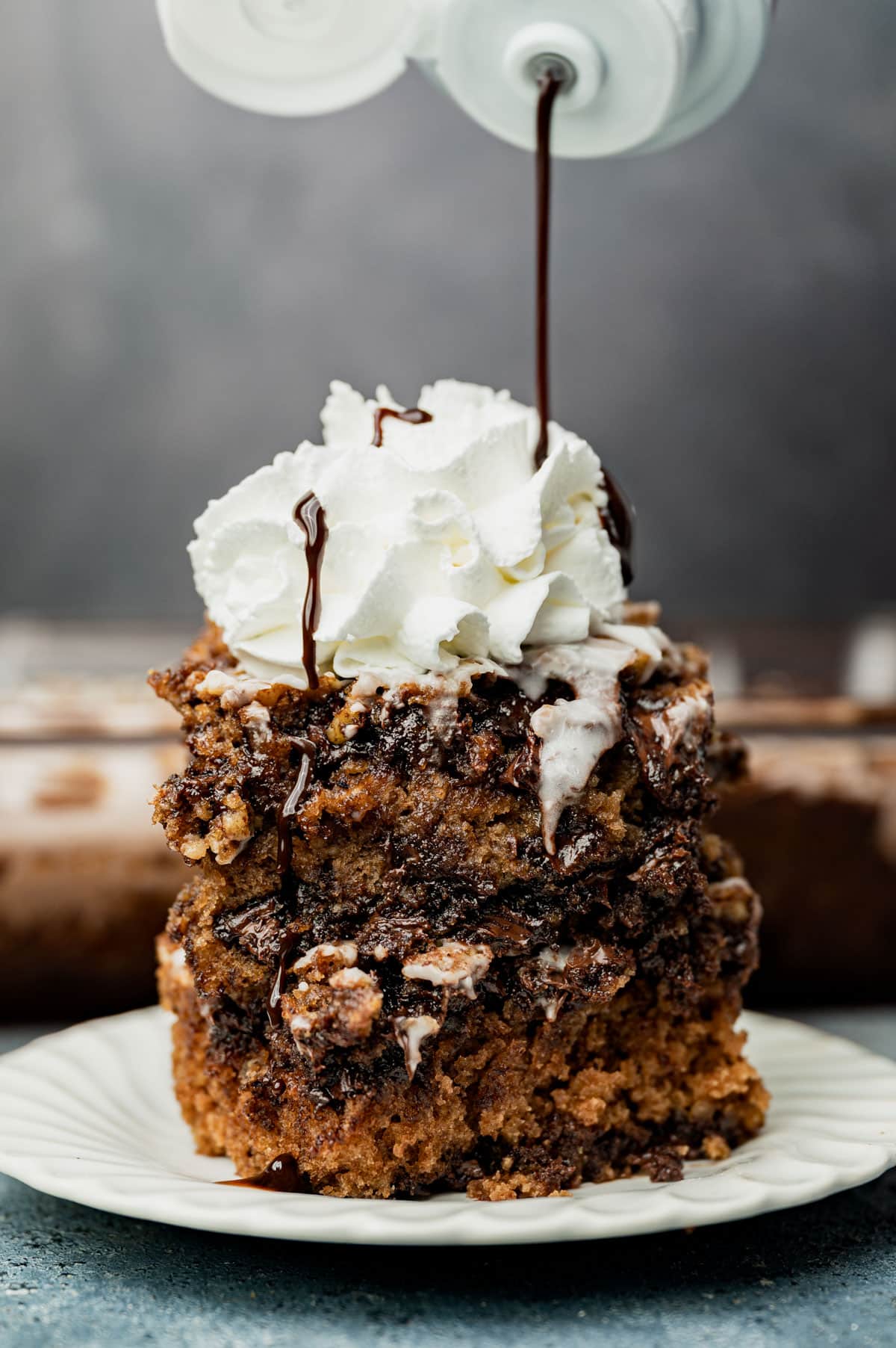 drizzling chocolate over chocolate chip oatmeal cake with whipped cream