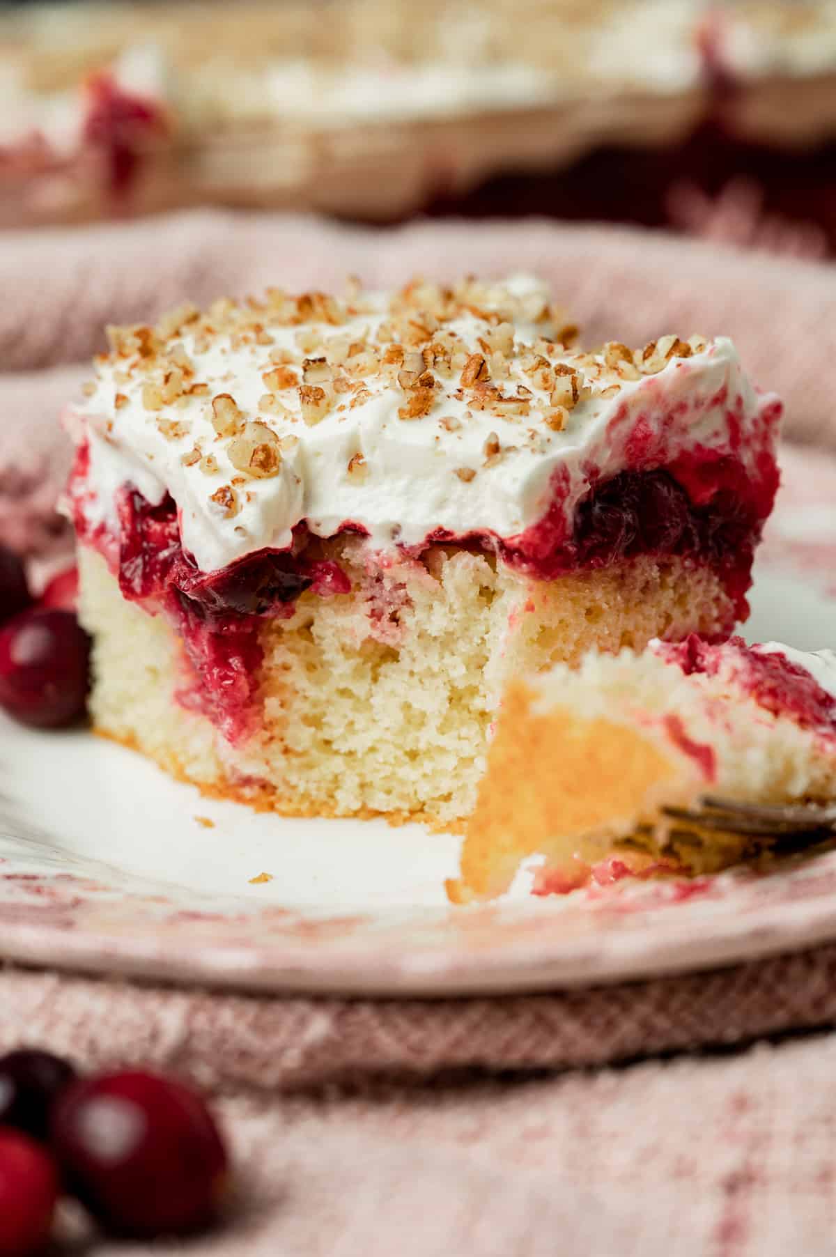 a piece of cranberry poke cake on a plate with a bite out