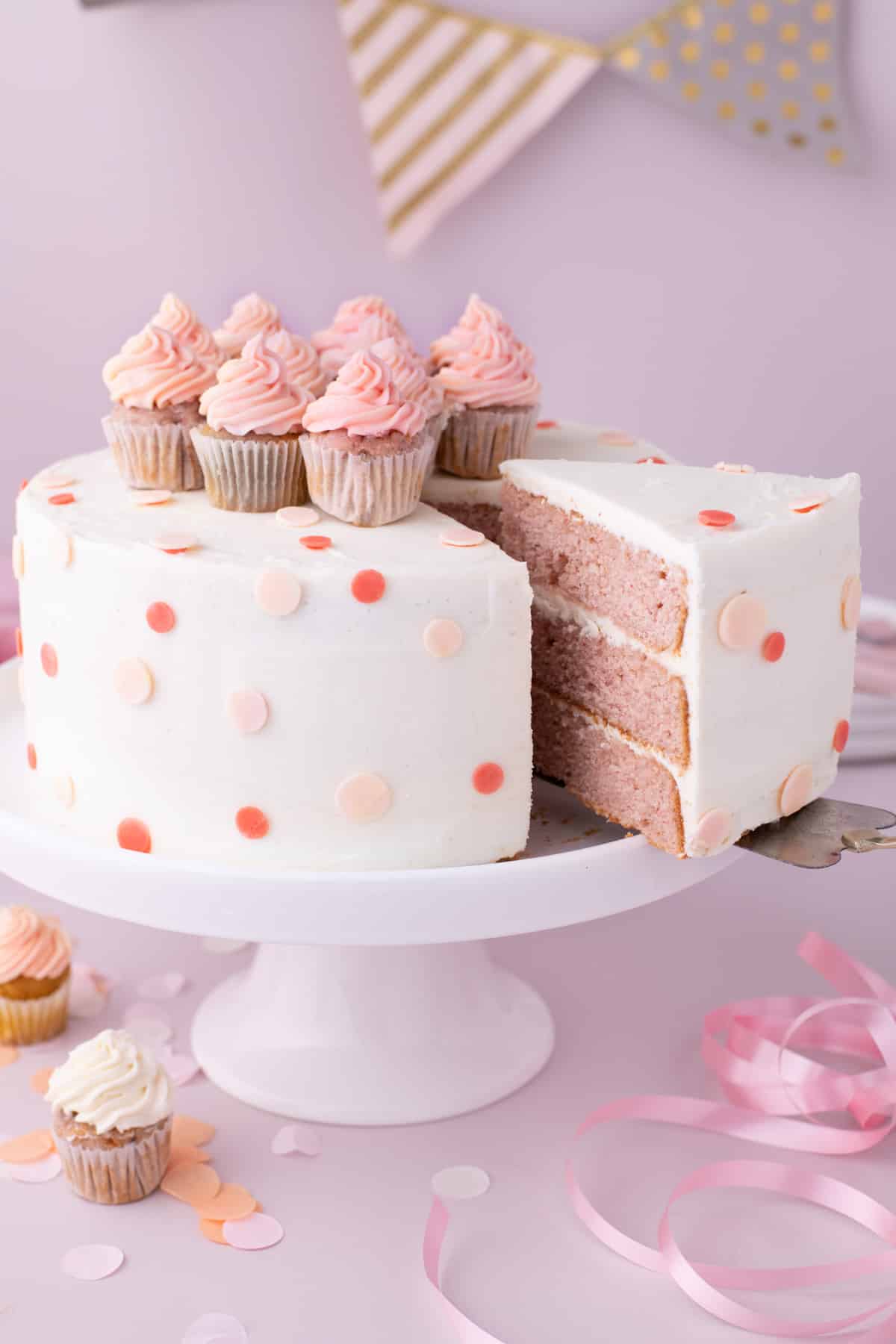 a frosted cake with mini cupcakes on top, with one slice on a spatula