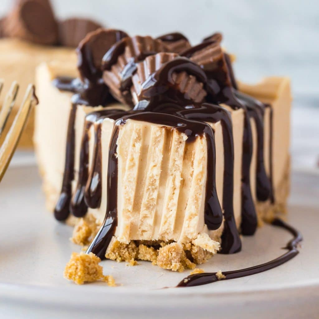 a piece of peanut butter cheesecake on a plate with fudge drizzled over the top and a bite out