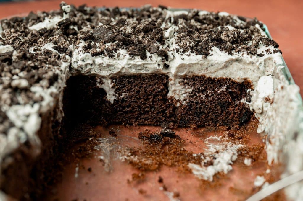an oreo poke cake in a cake pan with some pieces missing