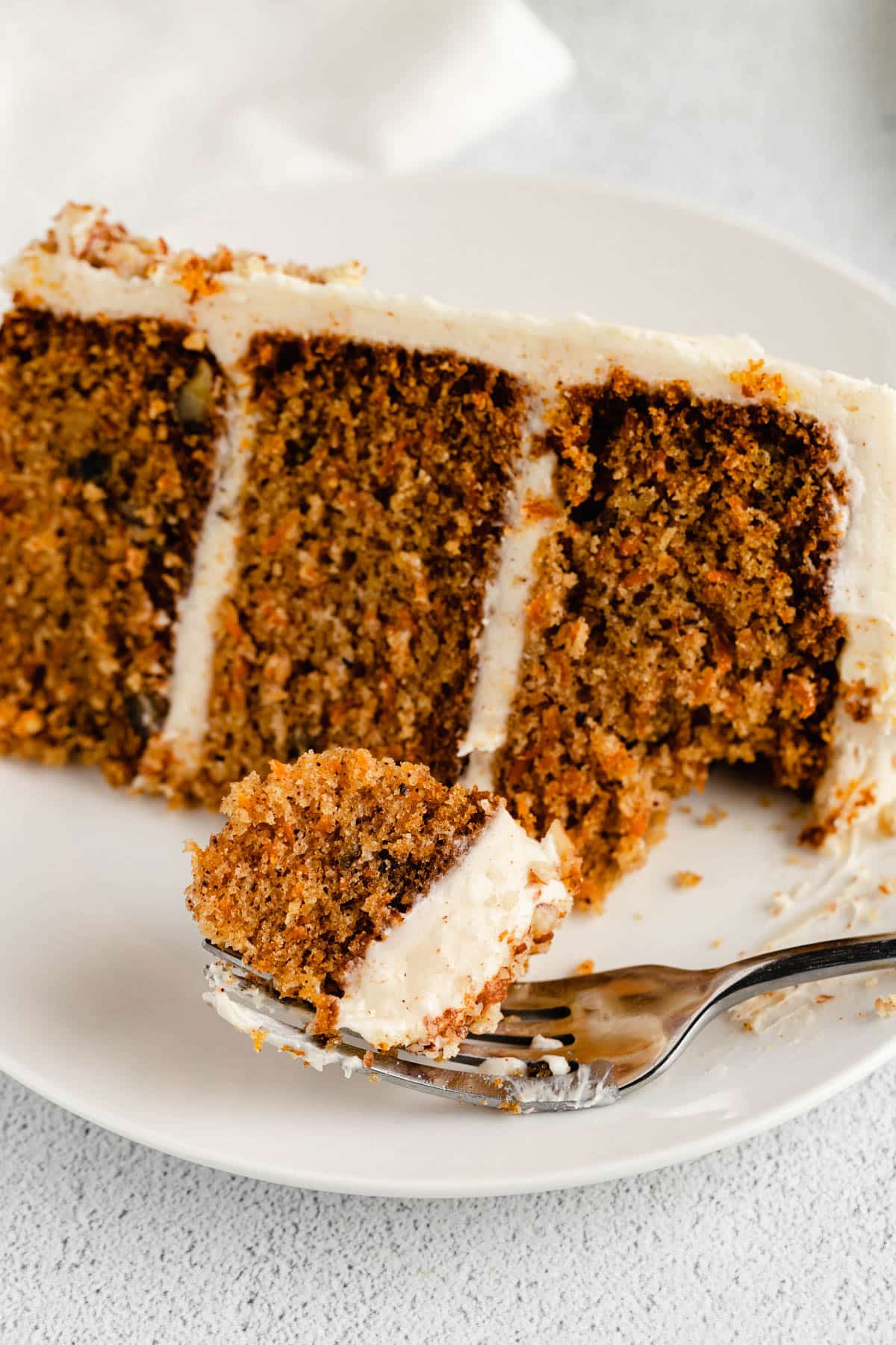 a piece of carrot cake on a plate with one bite on a fork