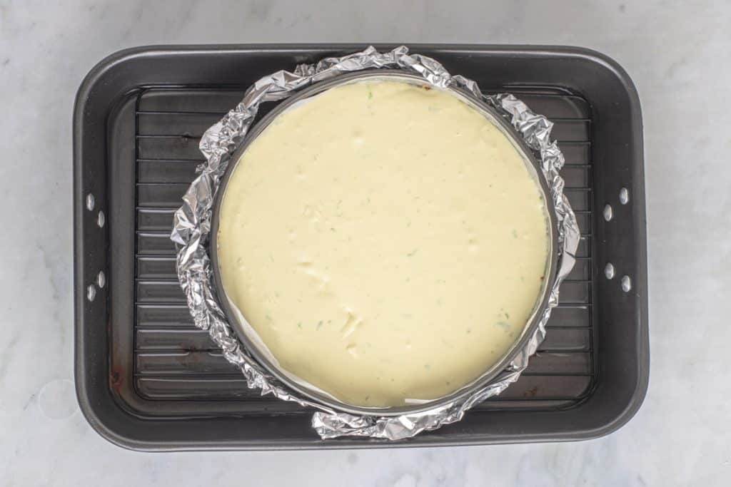 an unbaked cheesecake sitting in a water bath in a pan