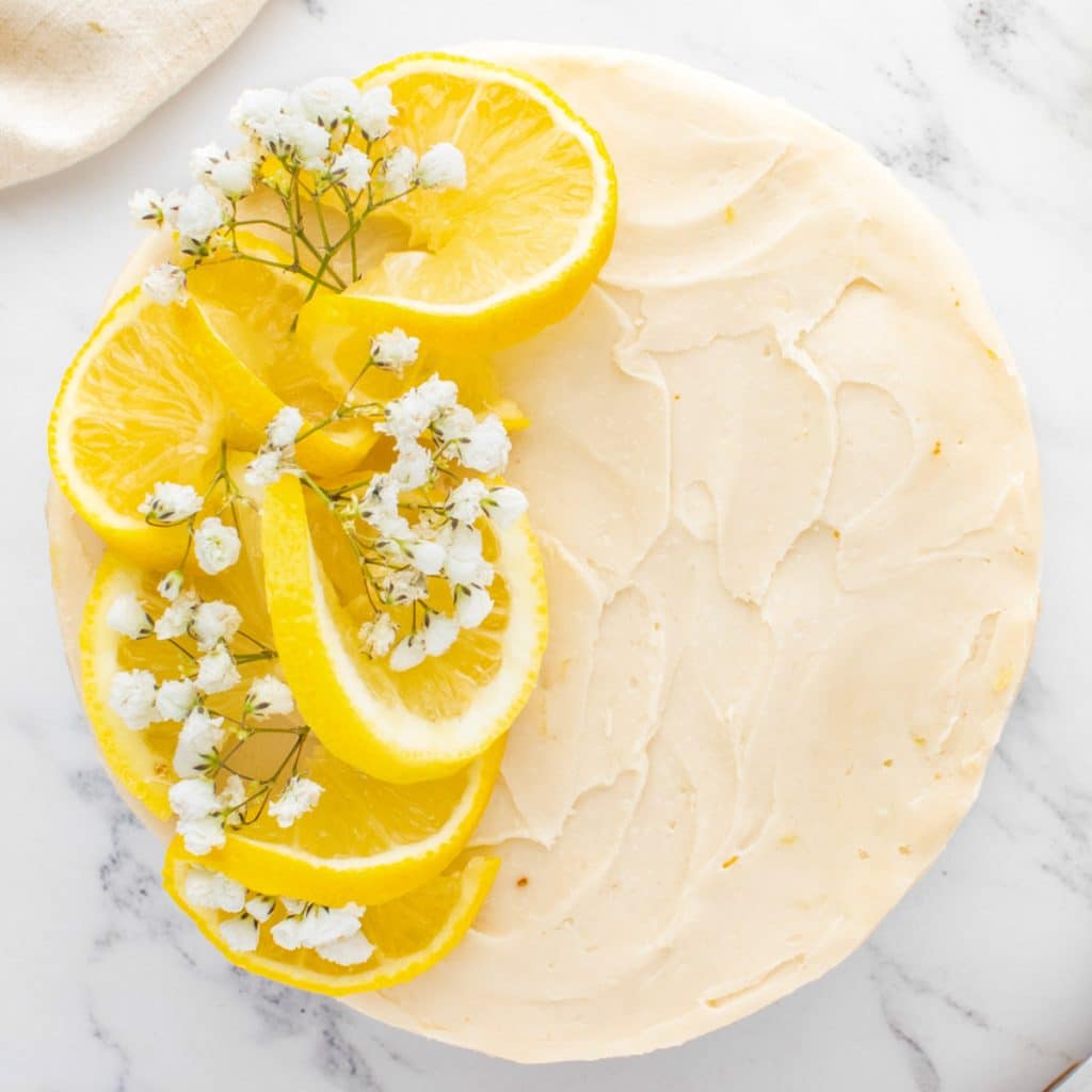 overhead view of a frosted cake with lemon slices and white flowers on top