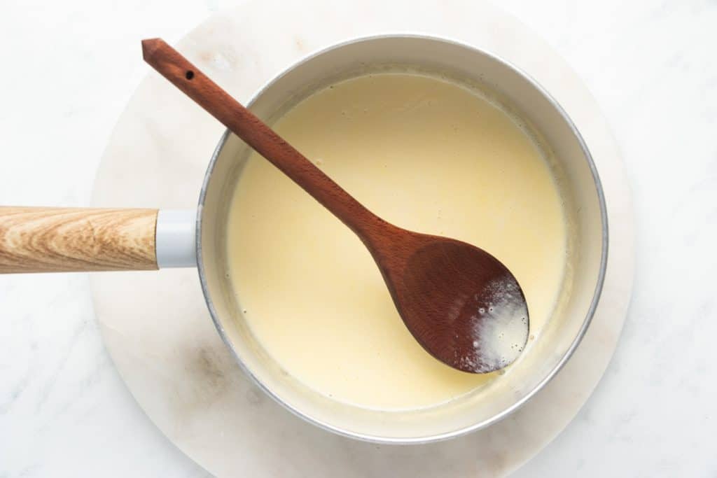 heavy cream in a saucepan with a wooden spoon